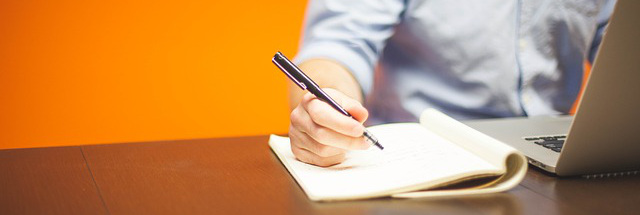 Man taking notes next to laptop.