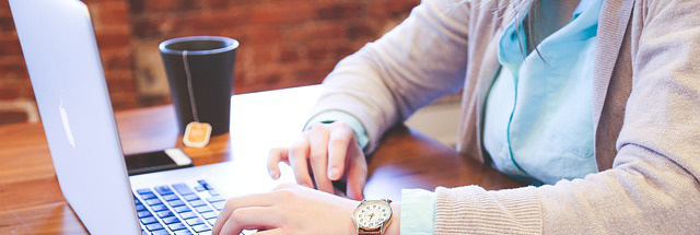 Woman typing with coffee mug nearby.